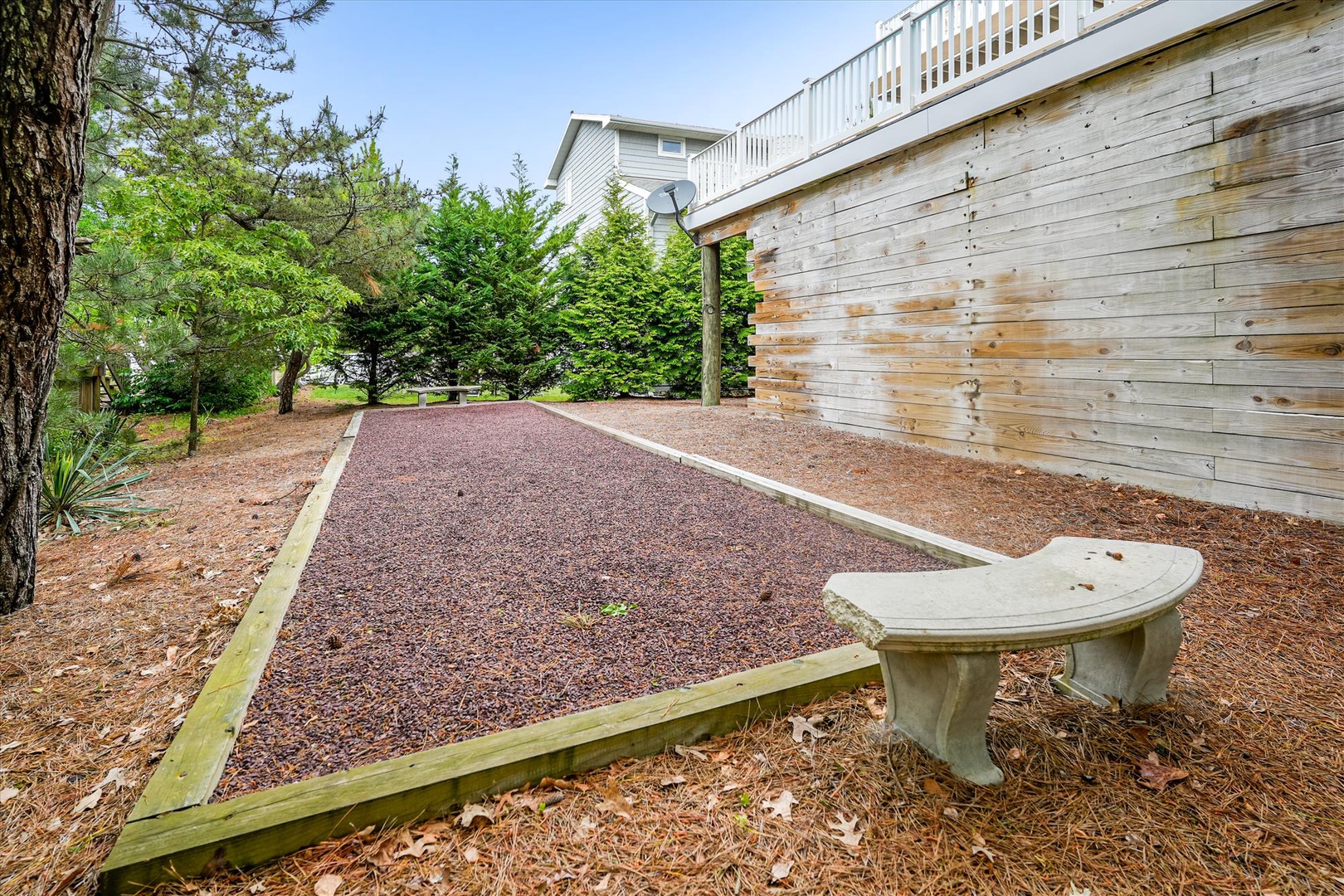 A peaceful outdoor area featuring a crushed stone court bordered by mature trees and a charming stone bench, perfect for quiet moments or outdoor games.