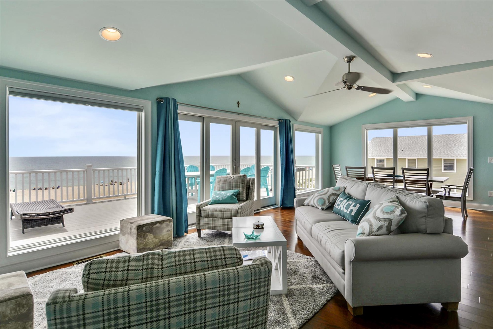Settle into this bright coastal living room, where calming aqua walls and ocean breezes through open doors invite you to relax on plush seating while taking in stunning beachfront views.