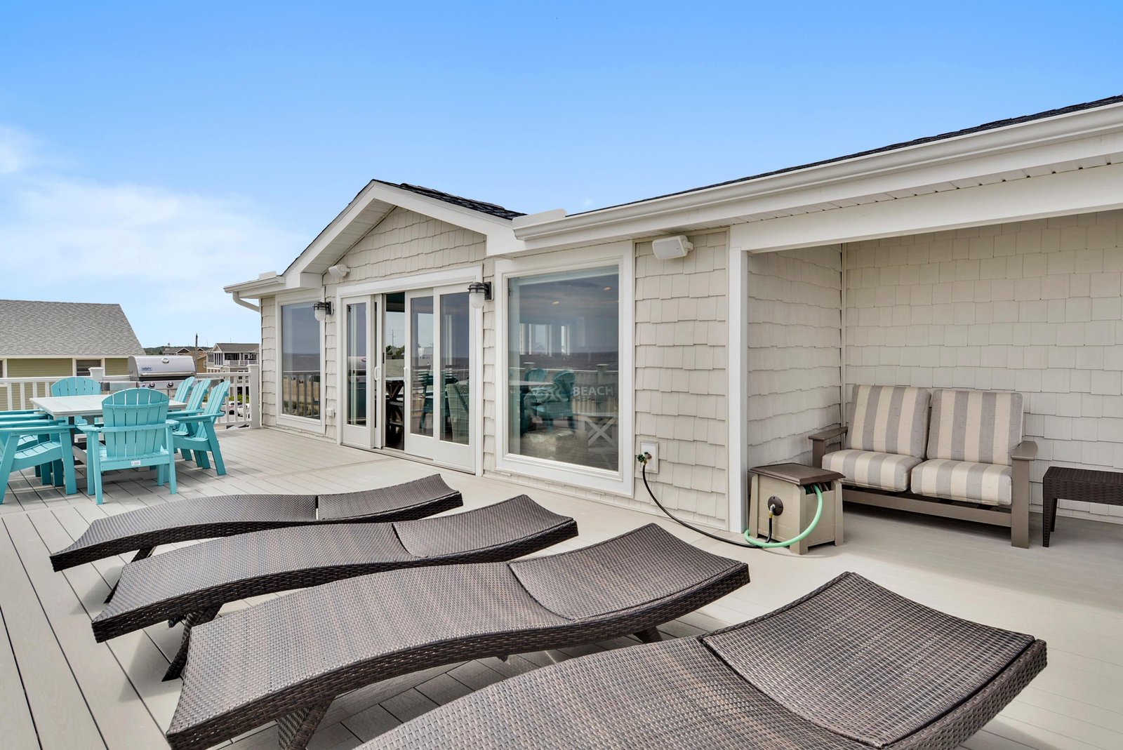 A spacious rooftop deck offers your perfect sunny retreat. Lounge on comfortable chairs, dine outdoors at turquoise seating, and unwind in coastal charm beneath open skies.