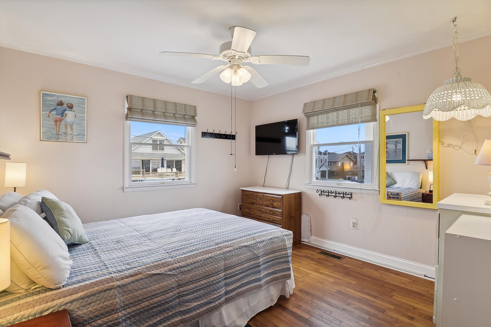 Unwind in this cozy bedroom with warm wood floors, soft natural light, and charming street views. Your peaceful retreat features a ceiling fan, mounted TV, and coastal-inspired décor to help you relax.