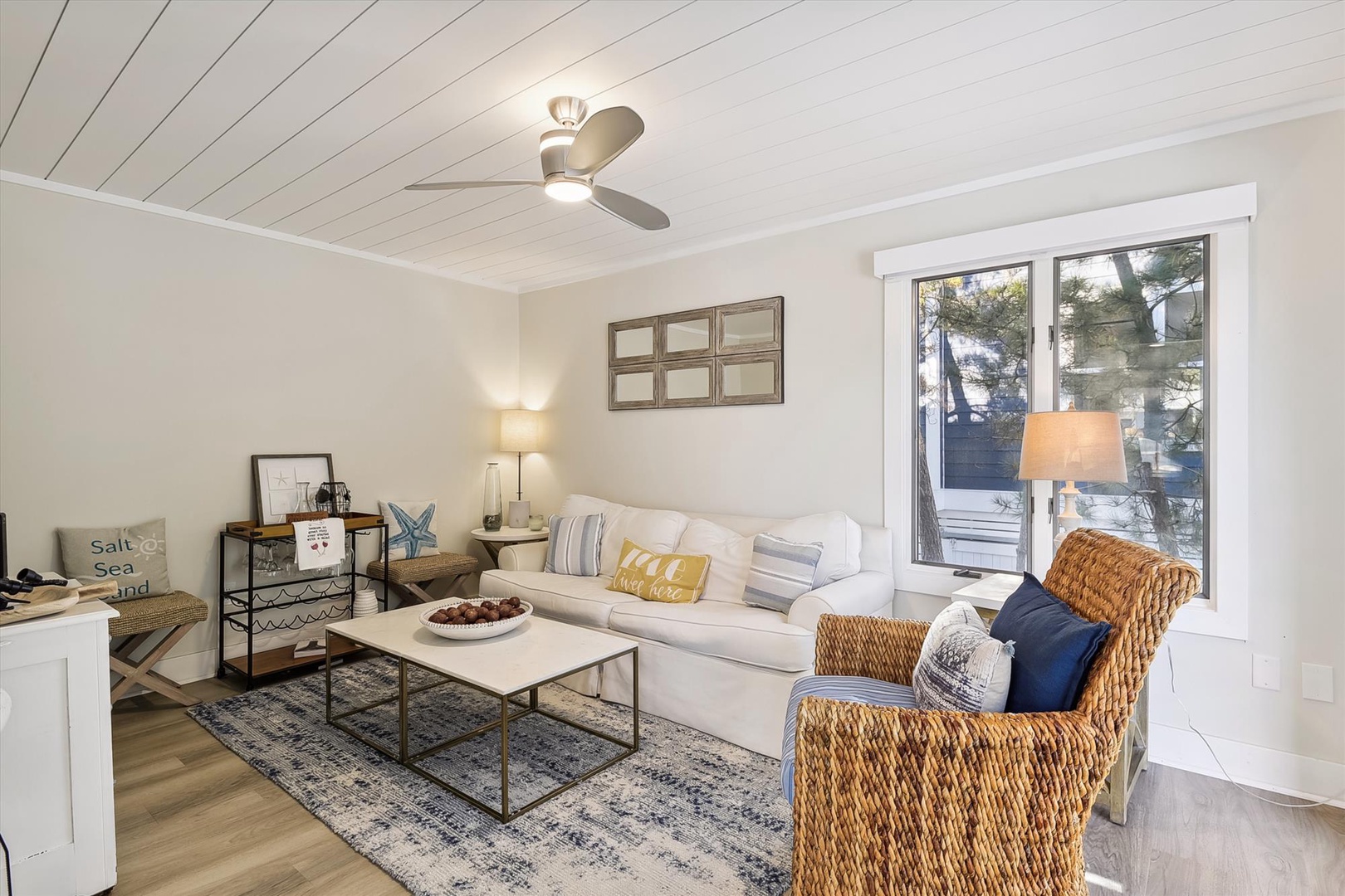 Sink into soft coastal comfort where natural light and beach-inspired touches make your perfect home base. The ceiling fan keeps you cool while you unwind with your favorite book in the woven armchair.
