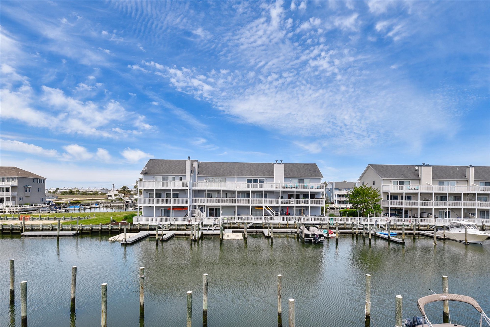 Waterfront townhouse community with private boat docks on calm marina waters beneath scenic cloud patterns.