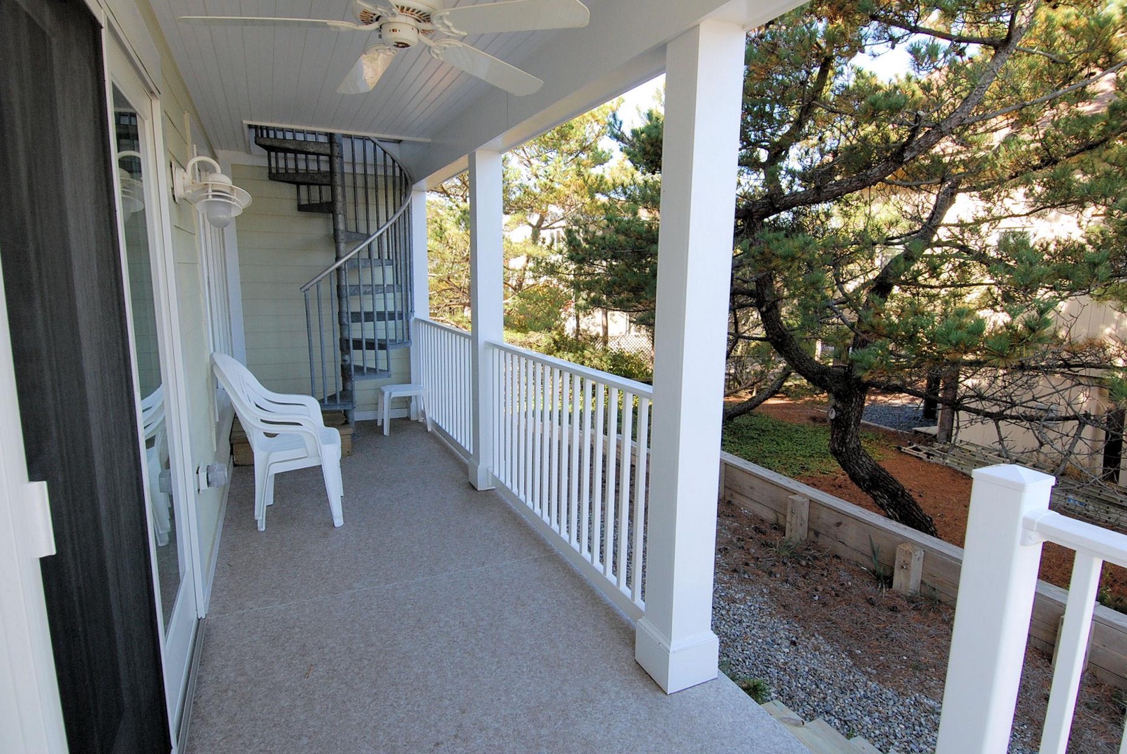 A covered balcony framed by tall pines creates your peaceful retreat, complete with seating and a spiral staircase connecting you to outdoor spaces below.