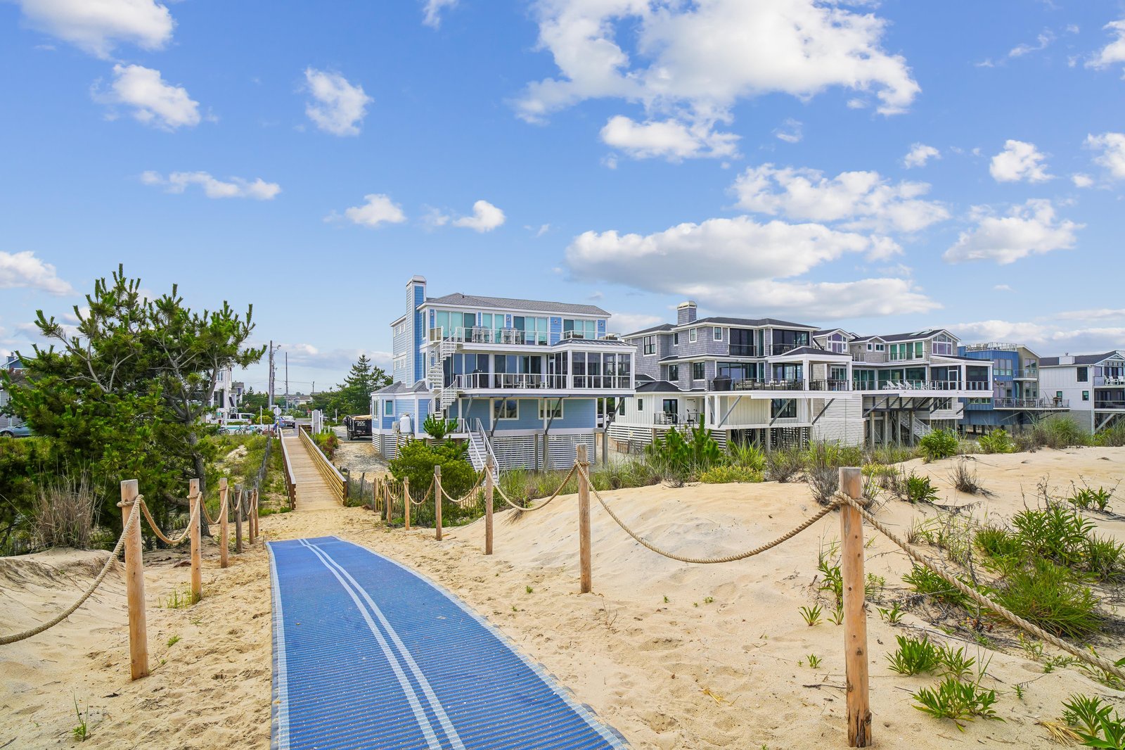 Beachfront property featuring accessible boardwalk leading directly to sandy shores, with coastal homes nestled among natural dunes under clear skies.
