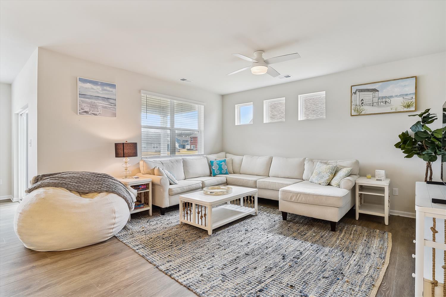 Sink into plush seating in your airy living room, where natural light, coastal art, and a ceiling fan create a breezy, welcoming retreat for gathering and relaxing.