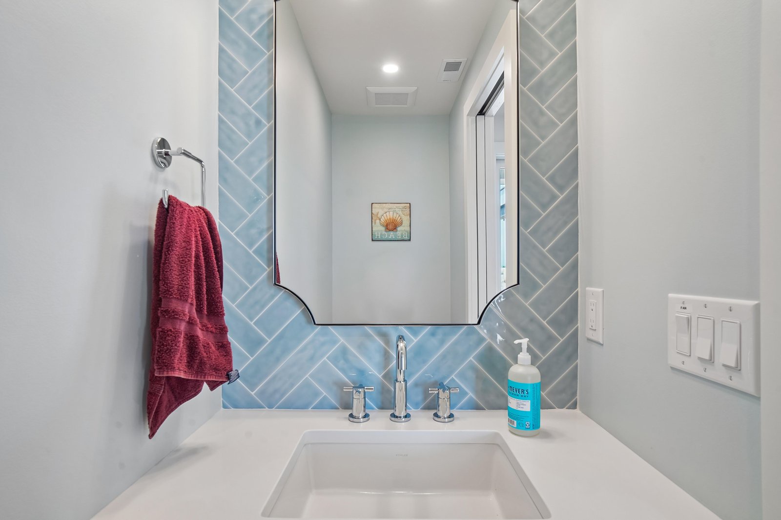 This bright coastal-inspired bathroom features a crisp white vanity and soft blue herringbone tile. You'll love the clean lines and beachy shell accent above the sink.