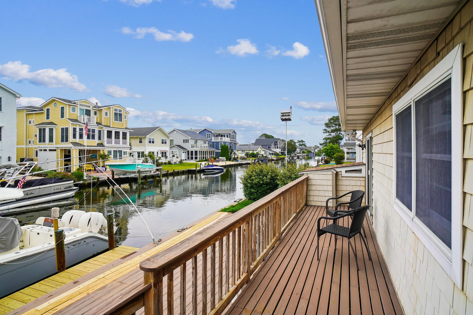 A private waterfront deck overlooks a tranquil marina lined with colorful homes and boats, offering a peaceful spot to relax and enjoy the coastal community views.