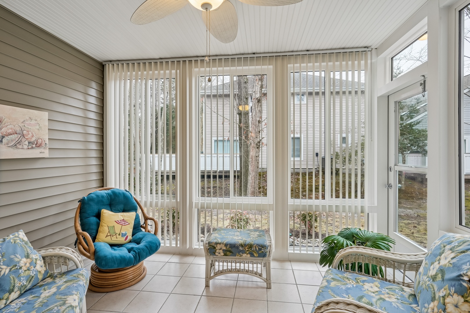 Relax in your sun-drenched enclosed porch with tropical furnishings and peaceful neighborhood views through floor-to-ceiling windows.