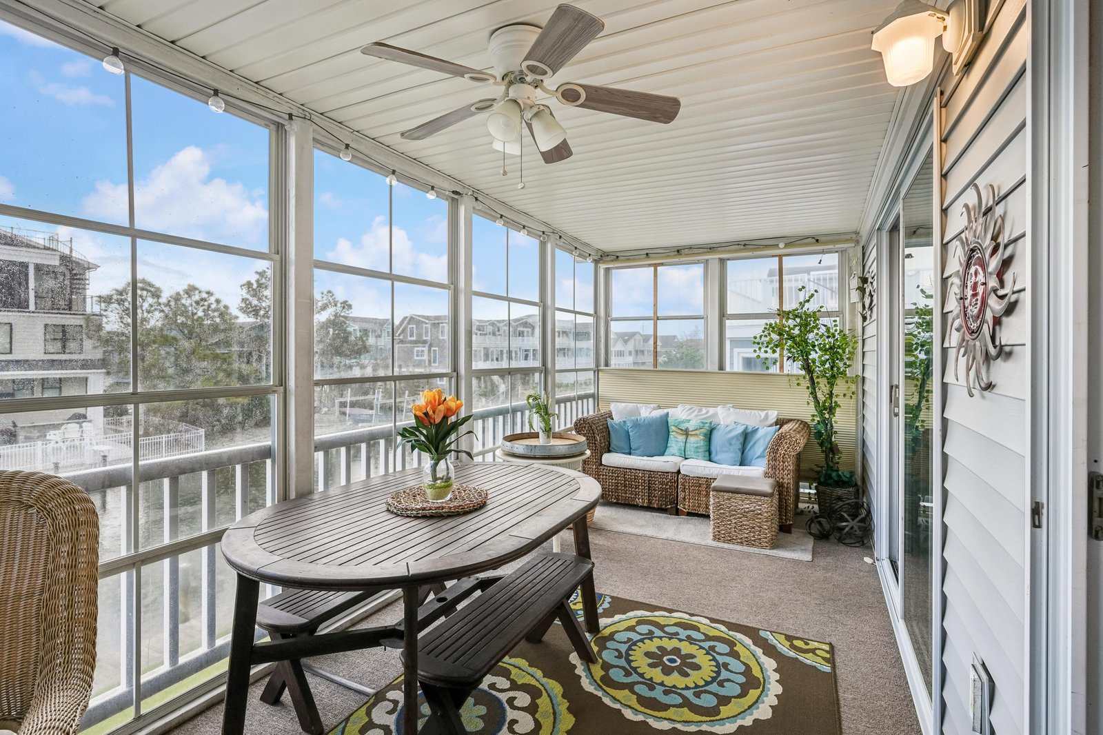 Imagine sipping your morning coffee here in this bright, enclosed sunroom, where ceiling fans keep you cool and cozy wicker seating invites long conversations overlooking the neighborhood.