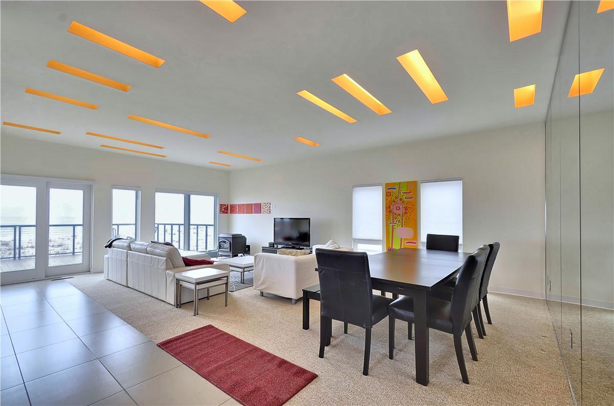 Step into an open living and dining space with striking modern design. Unique ceiling features cast a warm amber glow, while expansive windows frame bright views to help you relax and enjoy your retreat.