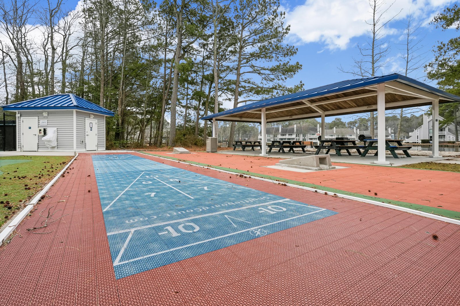 Communal recreational area features a shuffleboard court and covered picnic pavilion surrounded by pine trees.