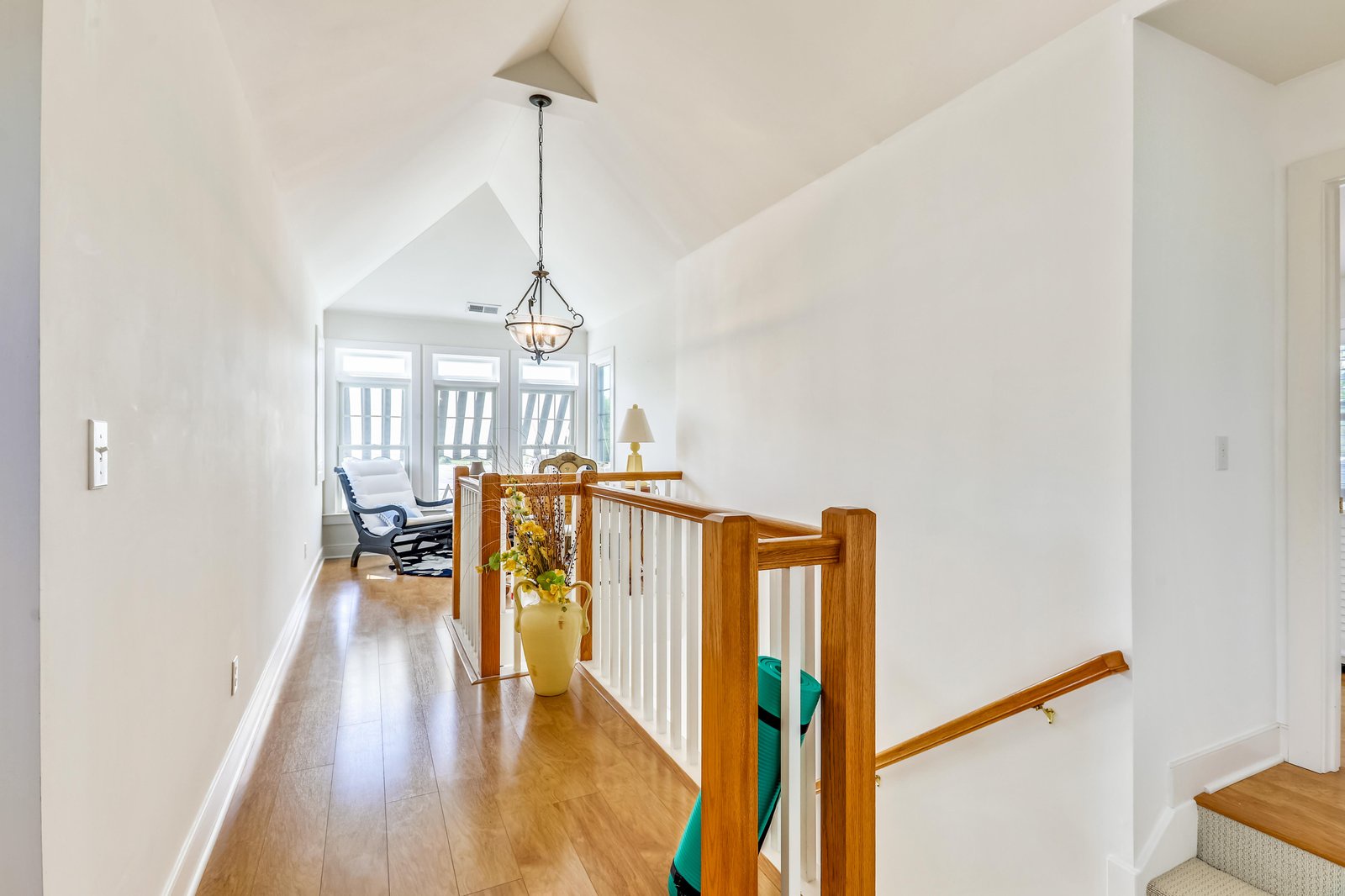 Bright upstairs hallway with soaring vaulted ceilings, warm wood floors, and a cozy reading nook bathed in natural light where you can curl up with a book.