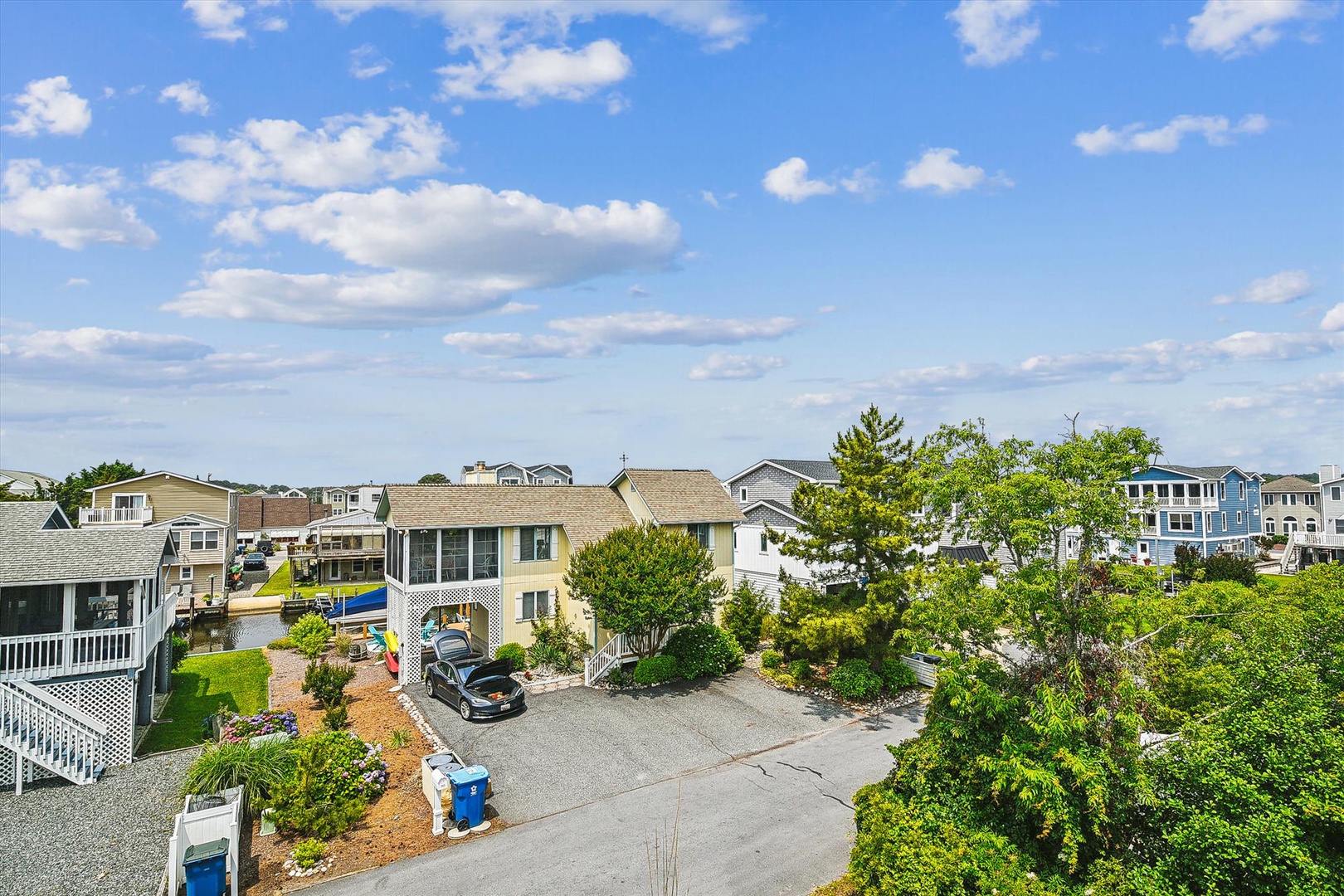 Aerial view of the property nestled in a charming residential neighborhood, surrounded by lush greenery and coastal homes. The property features ample parking and a peaceful setting just moments from the beach.