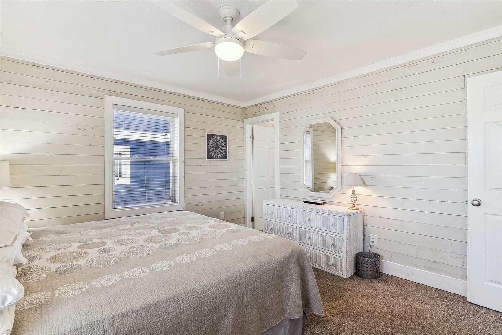 Picture yourself unwinding in this serene coastal bedroom with shiplap walls, plush bedding, and a gentle ceiling fan. Your perfect retreat awaits for restful nights.