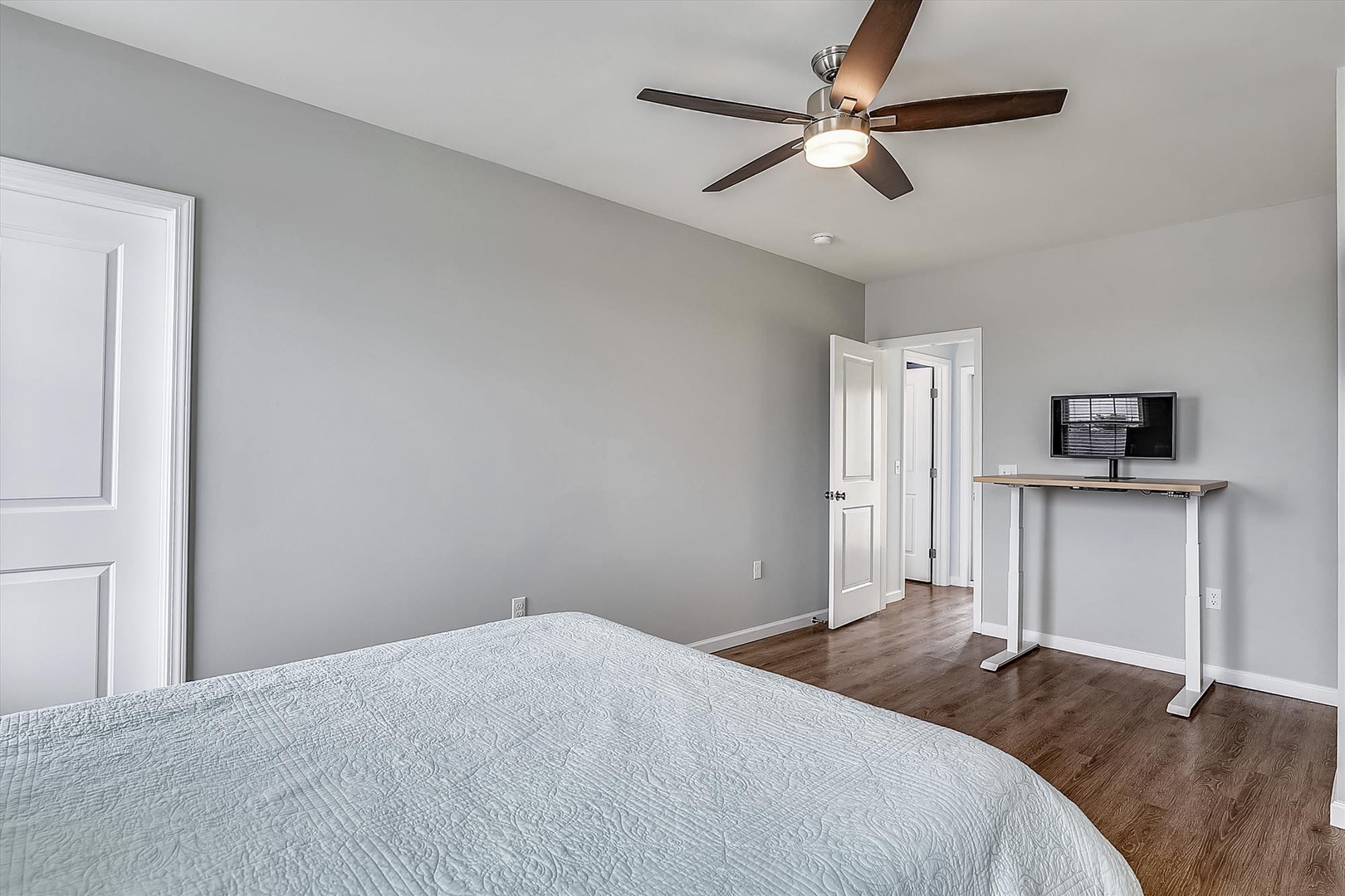 Drift off under a modern ceiling fan in your calming, light-filled bedroom featuring clean lines, warm wood floors, and a workspace perfect for planning your adventures.