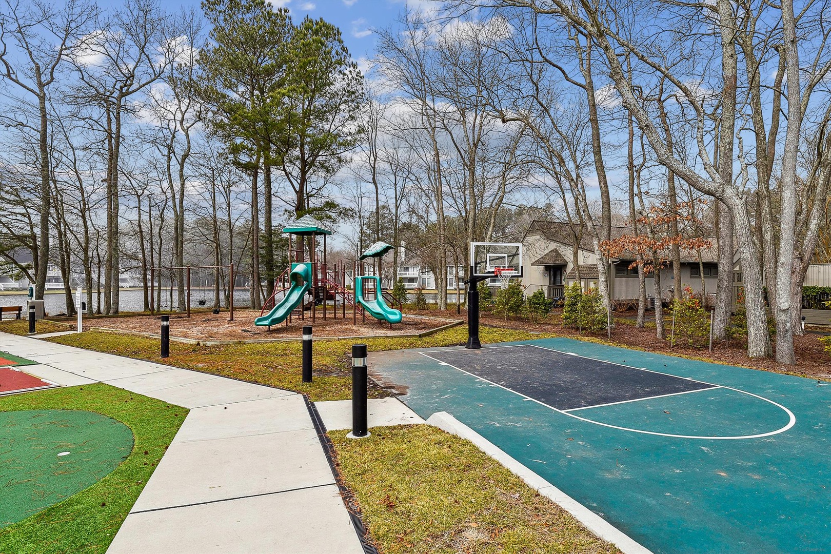 Family-friendly recreation area featuring playground equipment and basketball court surrounded by mature trees in a peaceful residential setting.