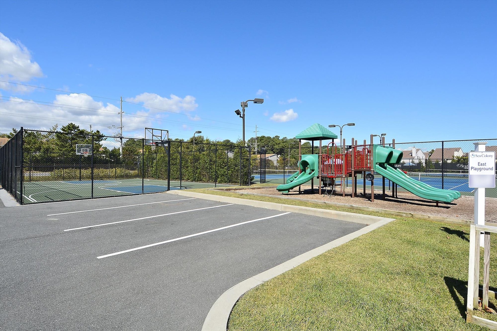 A sunny community setting featuring multiple recreational amenities including sports courts, playground slides, and parking area—all part of the surrounding neighborhood.