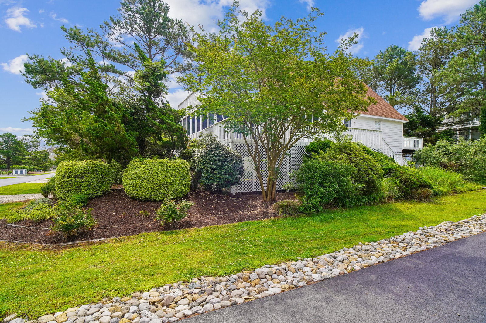 A charming white cottage-style property nestled among mature trees and professionally landscaped gardens in a peaceful residential neighborhood.