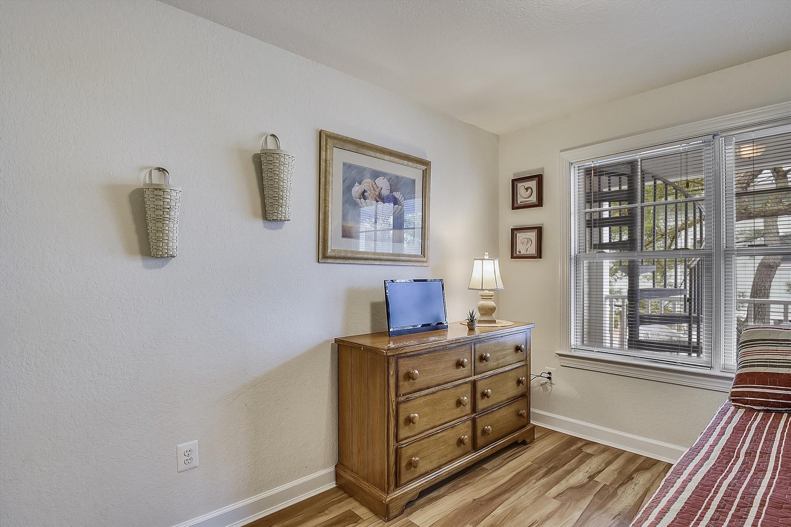 Your comfortable bedroom features warm wood furnishings, ample storage, and bright natural light streaming through large windows overlooking peaceful outdoor views.