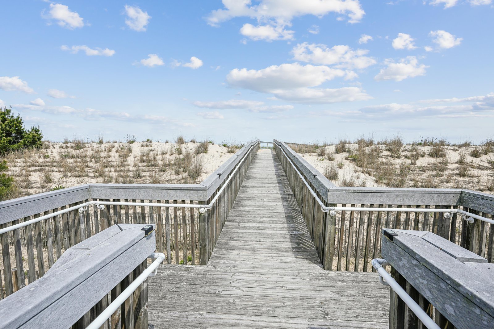A wooden boardwalk leads through natural coastal dunes toward sandy shores, offering easy beach access and scenic seaside surroundings.