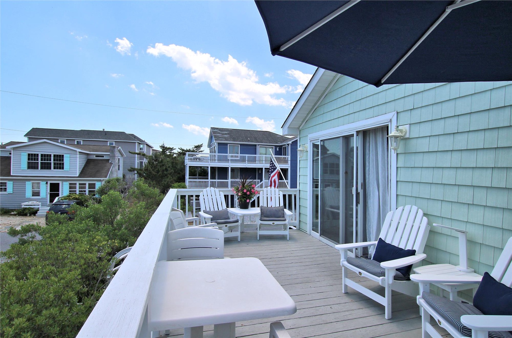 Spacious deck with comfortable lounge seating invites you to relax and soak up the coastal atmosphere, overlooking a charming neighborhood near the shore.