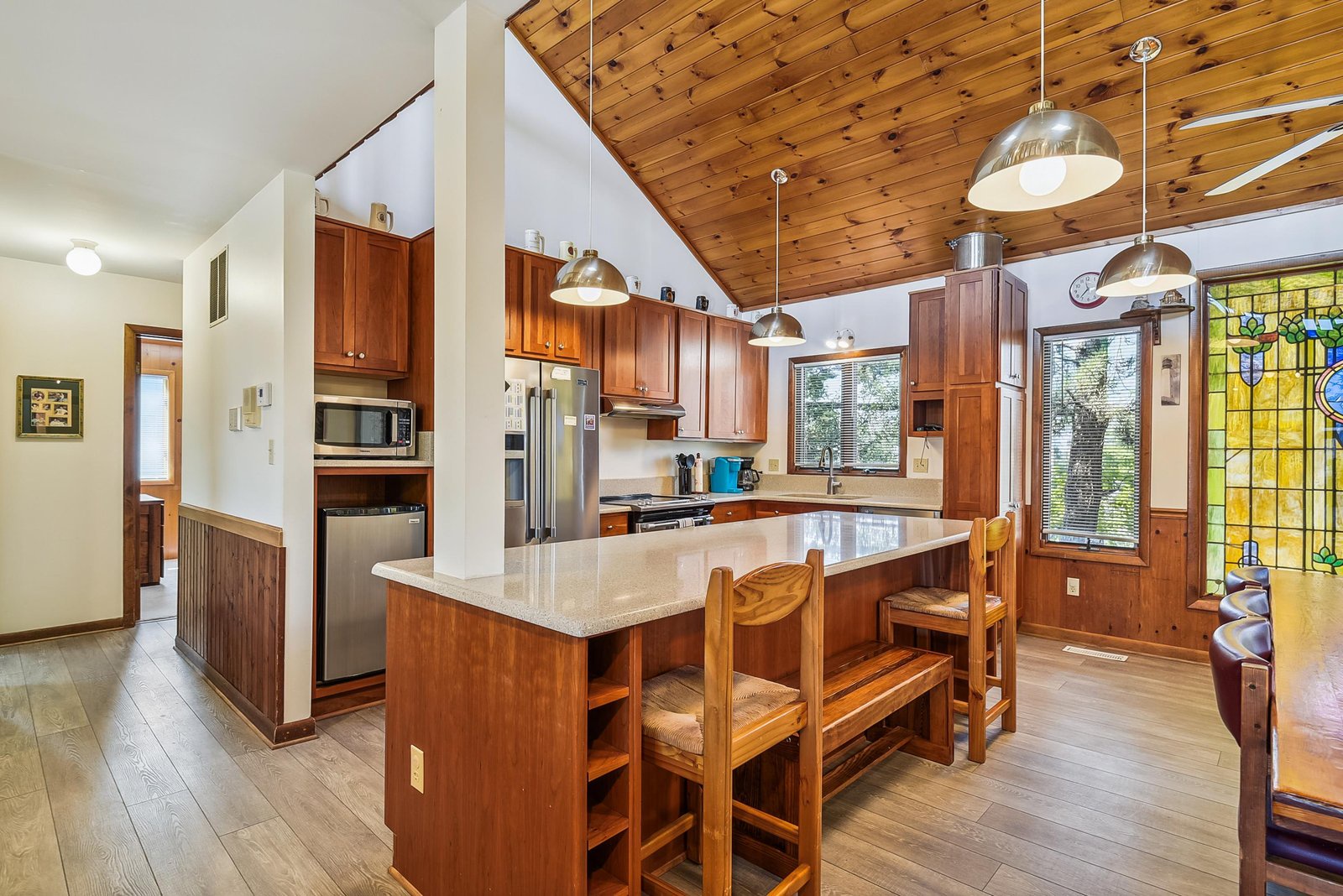 Spacious gourmet kitchen with rich wood cabinetry, stainless appliances, and a generous island for meal prep or dining. Natural light highlights the stunning wood ceiling.