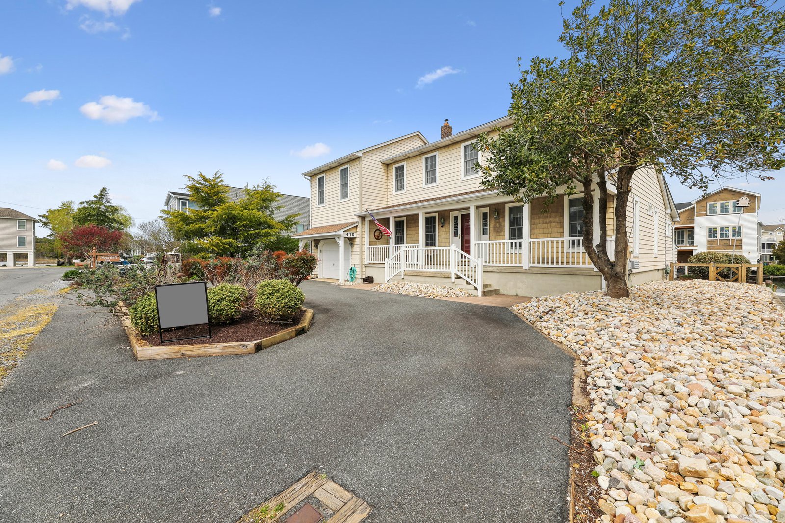 A welcoming beachside property with classic coastal charm, featuring a spacious wrap-around porch and private parking set among mature trees and landscaped gardens.