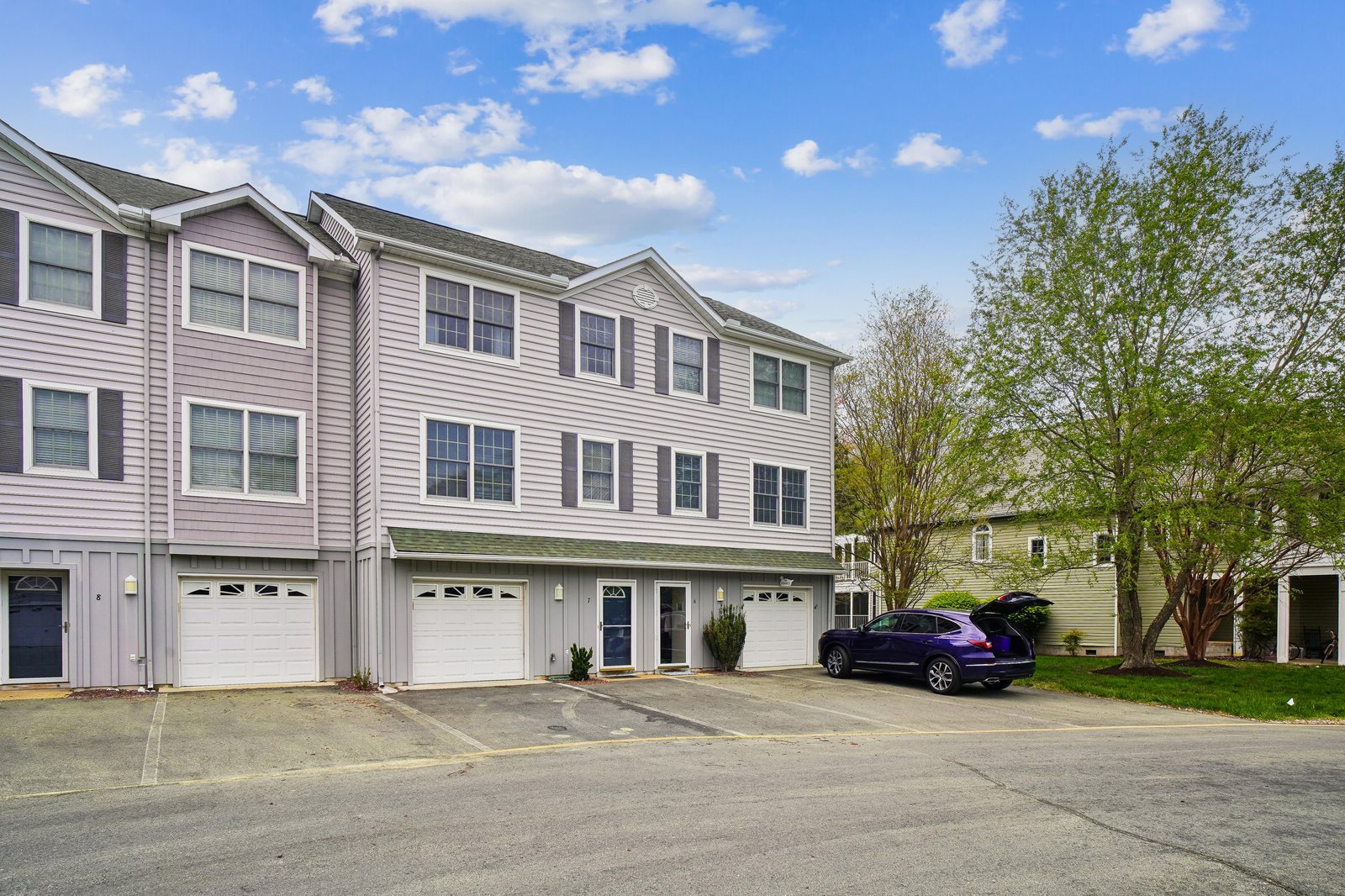 A residential townhome complex featuring ground-level garages and multiple units, set in a quiet area with mature trees and convenient parking for your stay.