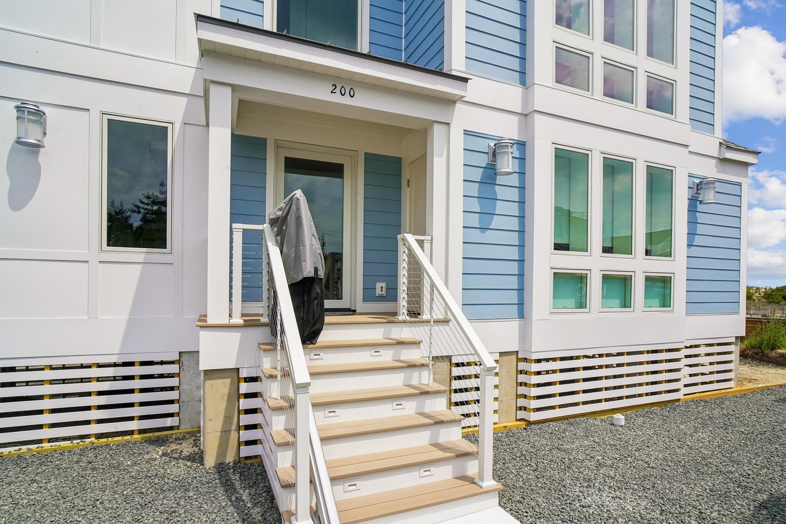 This contemporary beach cottage features a bright blue-and-white exterior with modern architectural details. The property is marked as unit 200 and sits in a quiet coastal neighborhood.