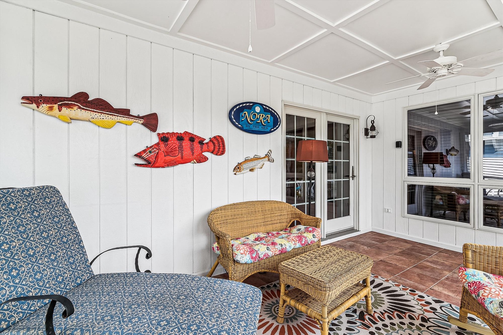 Bright, comfortable covered patio featuring playful coastal décor, wicker seating, and ceiling fan—ideal for unwinding after your adventures.