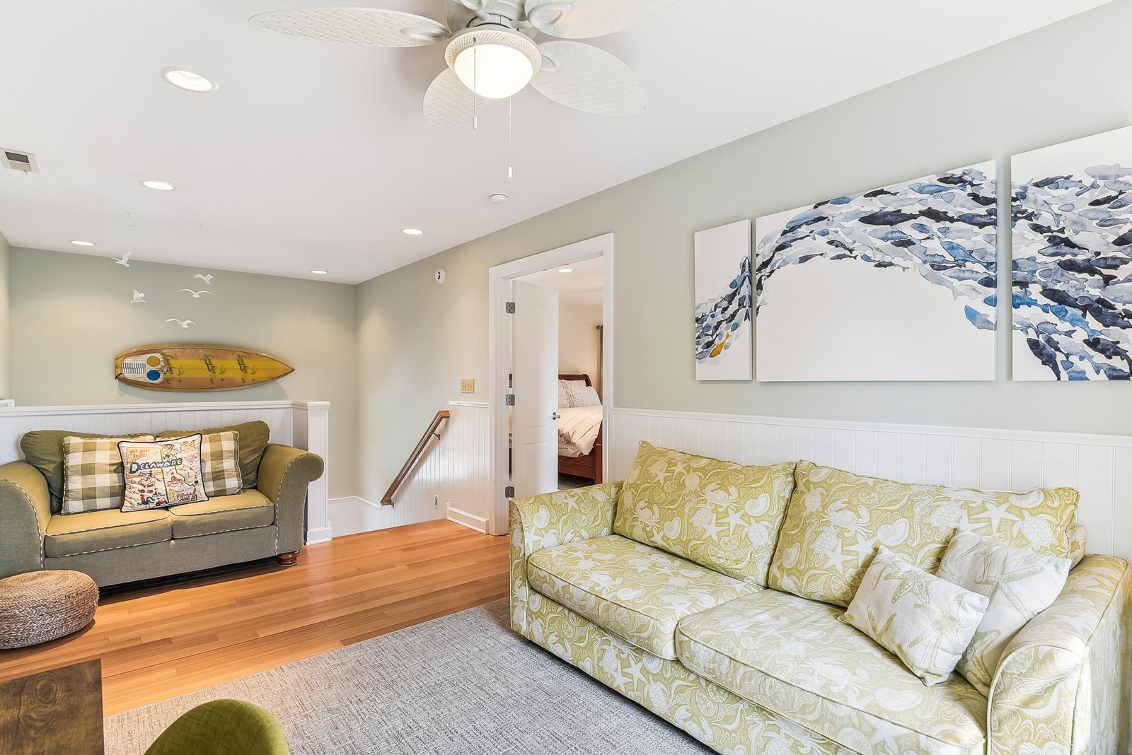 Settle into this bright coastal living space where soft greens and warm wood floors create your perfect beach getaway retreat.