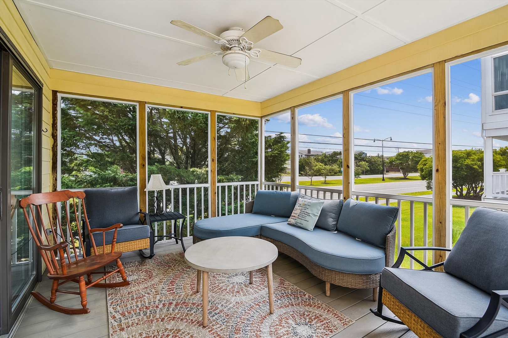 Sunlit enclosed porch with plush seating and ceiling fan, overlooking lush green surroundings—your perfect spot to unwind with morning coffee or an evening book.