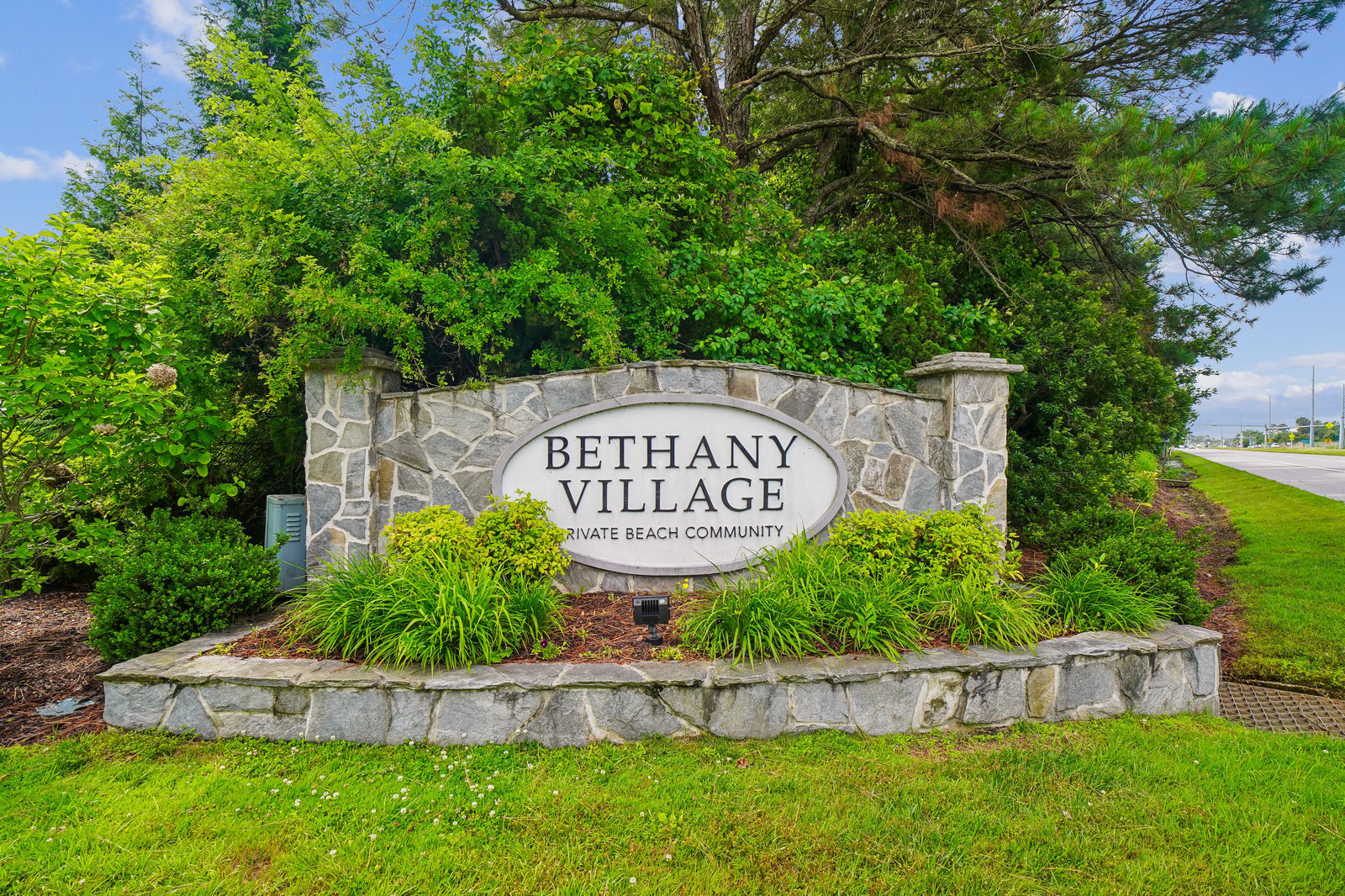 Bethany Village entrance marker welcomes guests to a private beach community, framed by lush landscaping and mature trees along the property's roadside location.