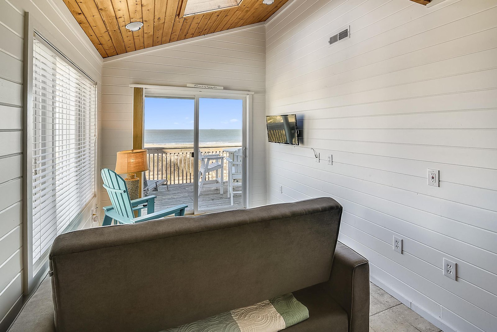 Settle into this cozy living space where bright shiplap walls meet warm wood ceilings. Through the glass doors, your private deck invites you to step out and enjoy the ocean breeze and sandy shore just beyond.