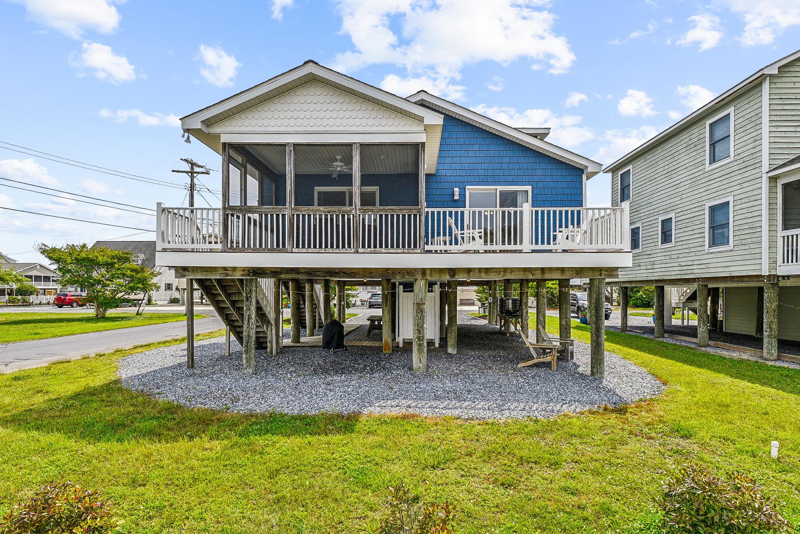 This charming blue coastal cottage features a screened porch and elevated deck on stilts, offering a classic beach-town feel in a friendly neighborhood setting perfect for a laid-back getaway.