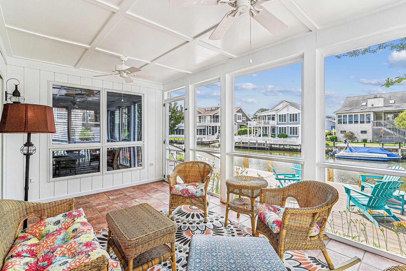 Settle into your private sunroom where wicker seating and cheerful cushions invite you to unwind. Through wide windows, you'll catch views of the waterway and neighboring homes—a perfect spot for morning coffee or evening relaxation.