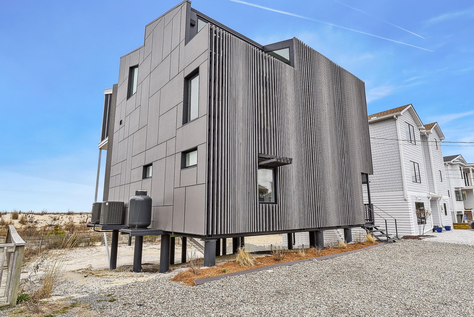Modern coastal architecture elevated on stilts, just steps from sandy dunes—a striking beachside retreat on a peaceful shore.