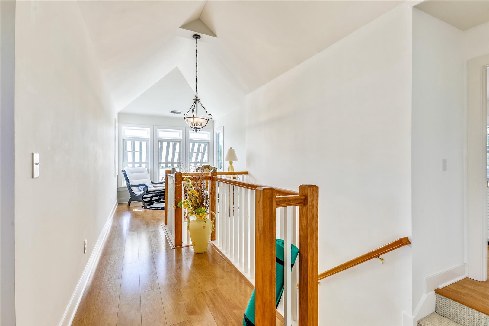 Bright hallway with soaring vaulted ceilings and warm wood floors leads to a peaceful seating nook where you can unwind with morning coffee and natural light.