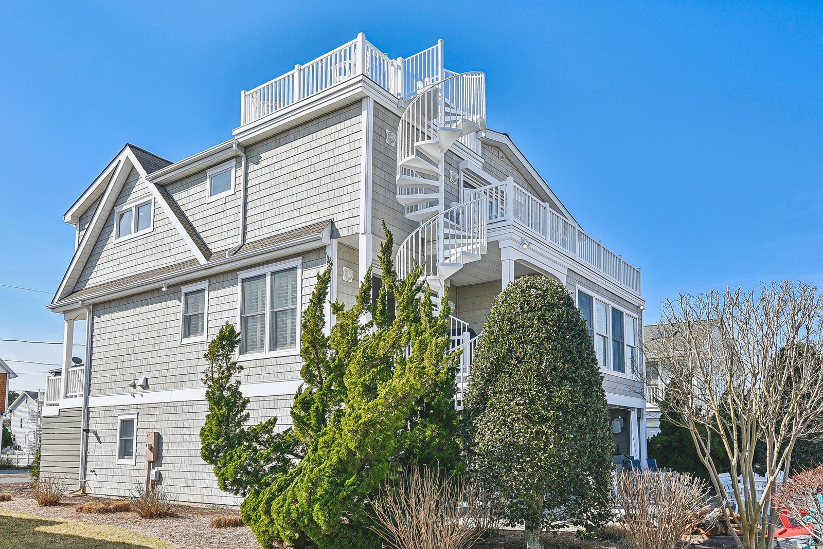 A coastal vacation home in a residential neighborhood, featuring a private rooftop deck accessed by spiral staircase for elevated views of the surrounding area.