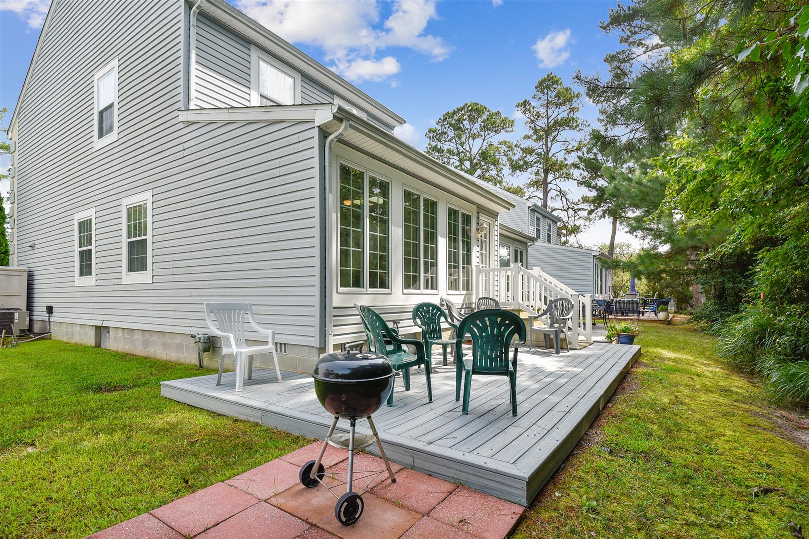 Modern vacation home with spacious deck, outdoor seating, and BBQ grill set among mature trees in a peaceful neighborhood—perfect for your getaway.