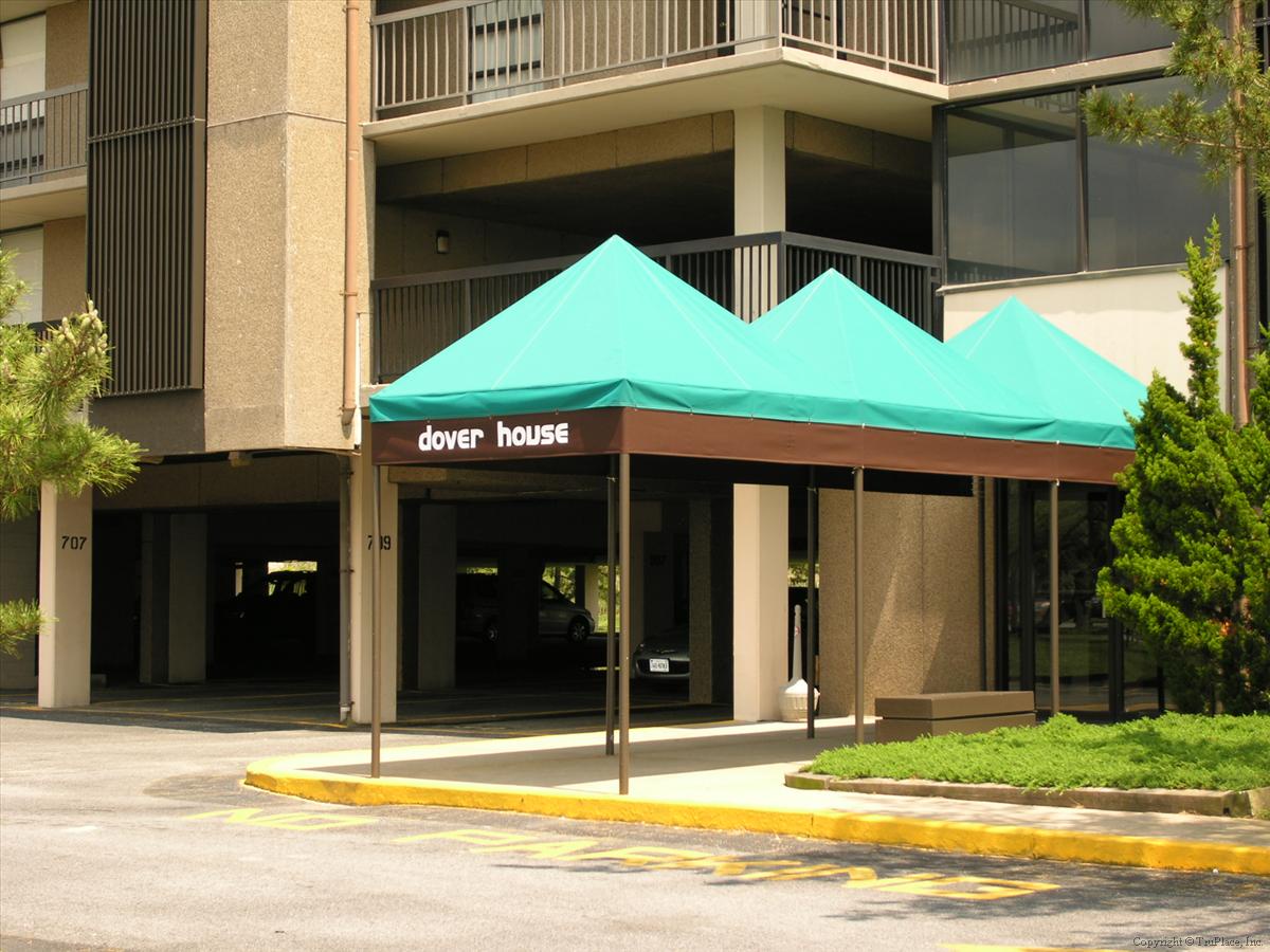 The Dover House entrance stands sheltered under distinctive turquoise awnings, surrounded by landscaped greenery and featuring convenient covered access and on-site parking.