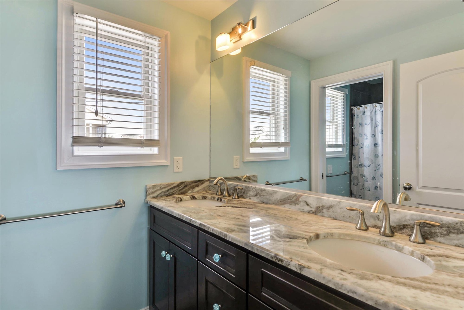 Step into your spa-like bathroom retreat with dual sinks, elegant marble countertops, and soft natural light streaming through the window. A refreshing space to start your day feeling pampered and relaxed.