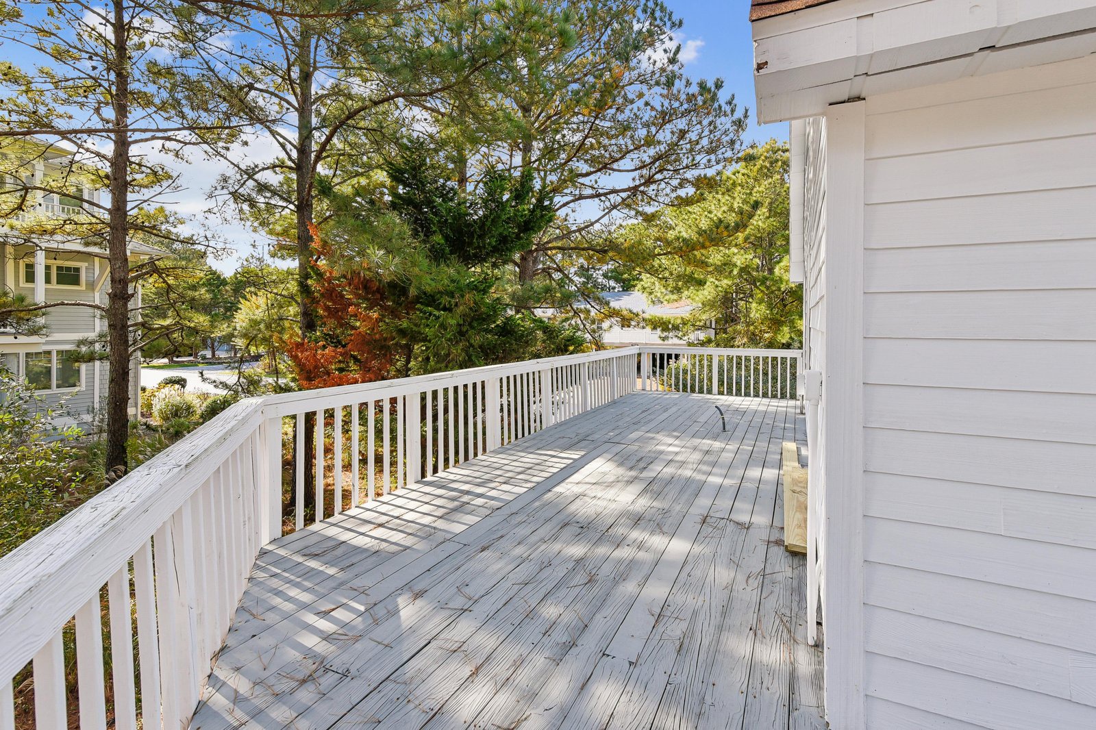A spacious wrap-around deck overlooking a peaceful neighborhood, ideal for morning coffee or evening relaxation surrounded by tall pines and autumn foliage.