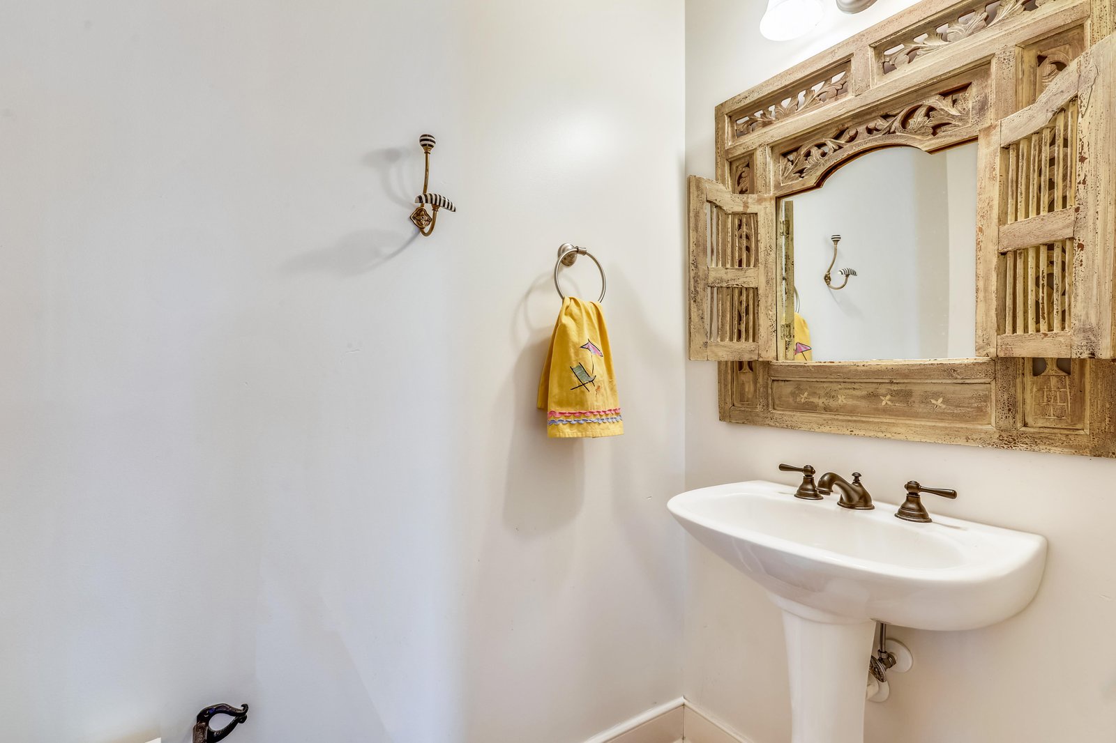 Freshen up in your charming bathroom, where a rustic carved-wood mirror and classic pedestal sink create a warm, welcoming retreat.