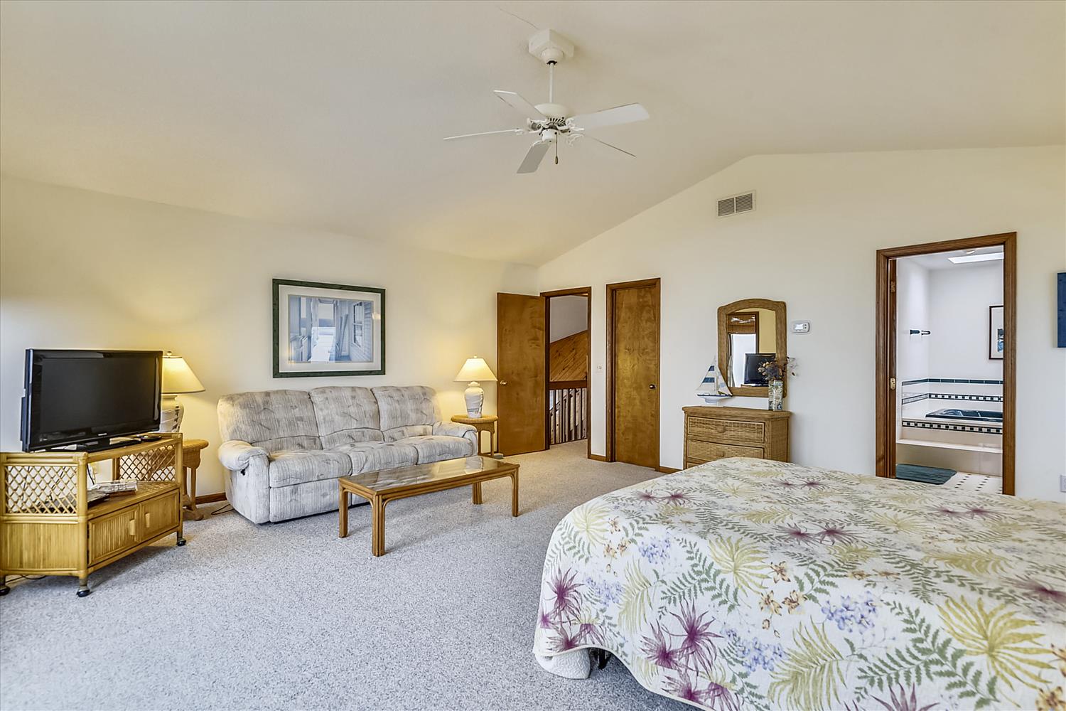 Unwind in your spacious bedroom with a cozy seating area and gentle ceiling fan. The soft carpet and homey furnishings create a peaceful haven for relaxation.