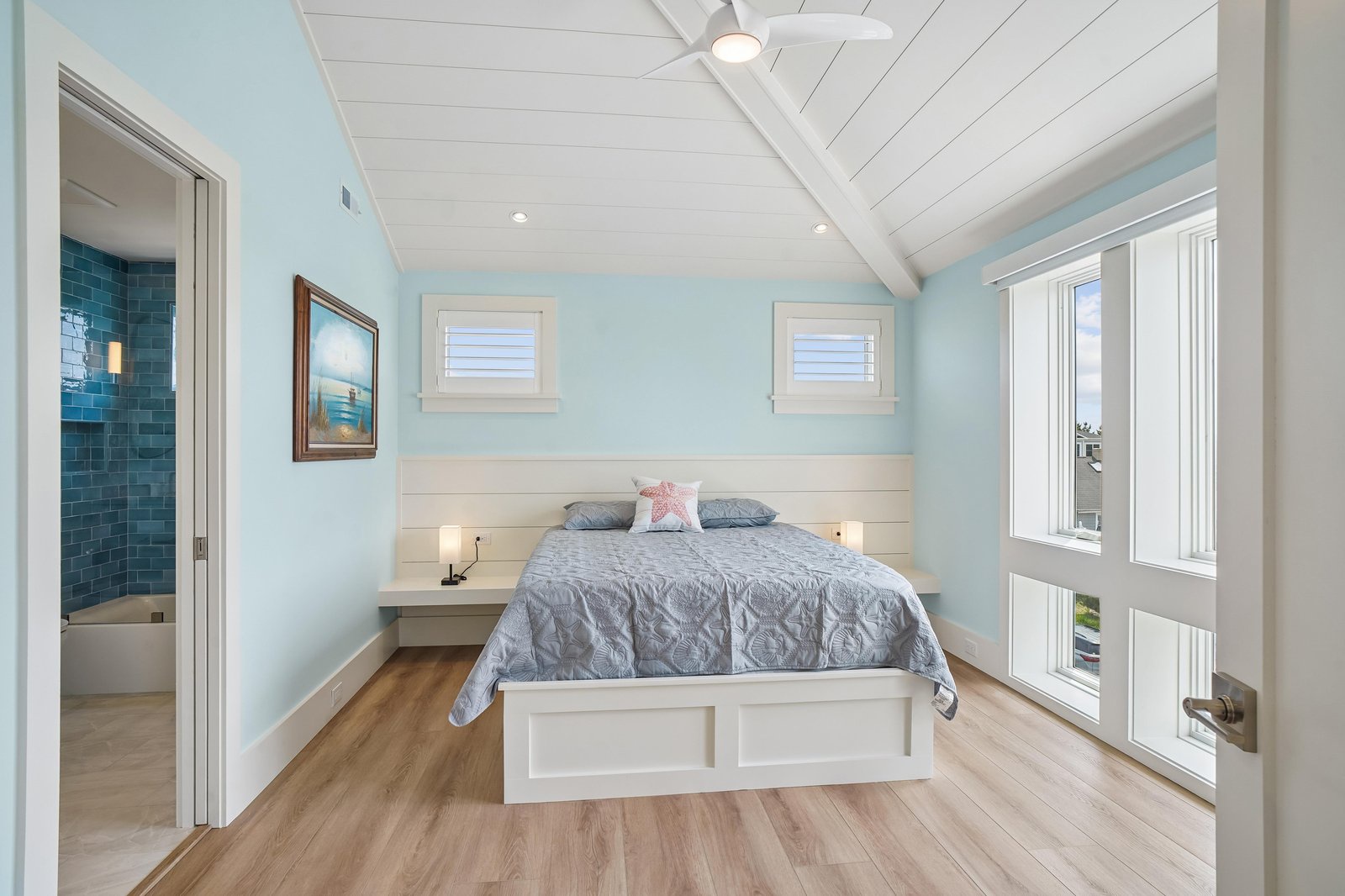 Wake up in your serene coastal bedroom with vaulted shiplap ceilings, soft blue walls, and natural light spilling through bright windows, setting a calm and refreshing tone for your stay.