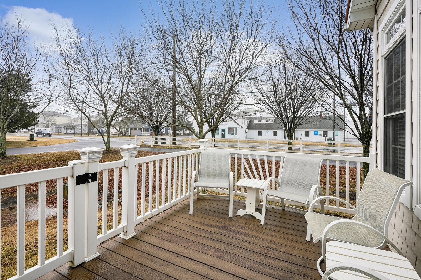 A spacious deck overlooks a peaceful residential neighborhood, framed by mature trees and surrounded by nearby homes in a quiet community setting.