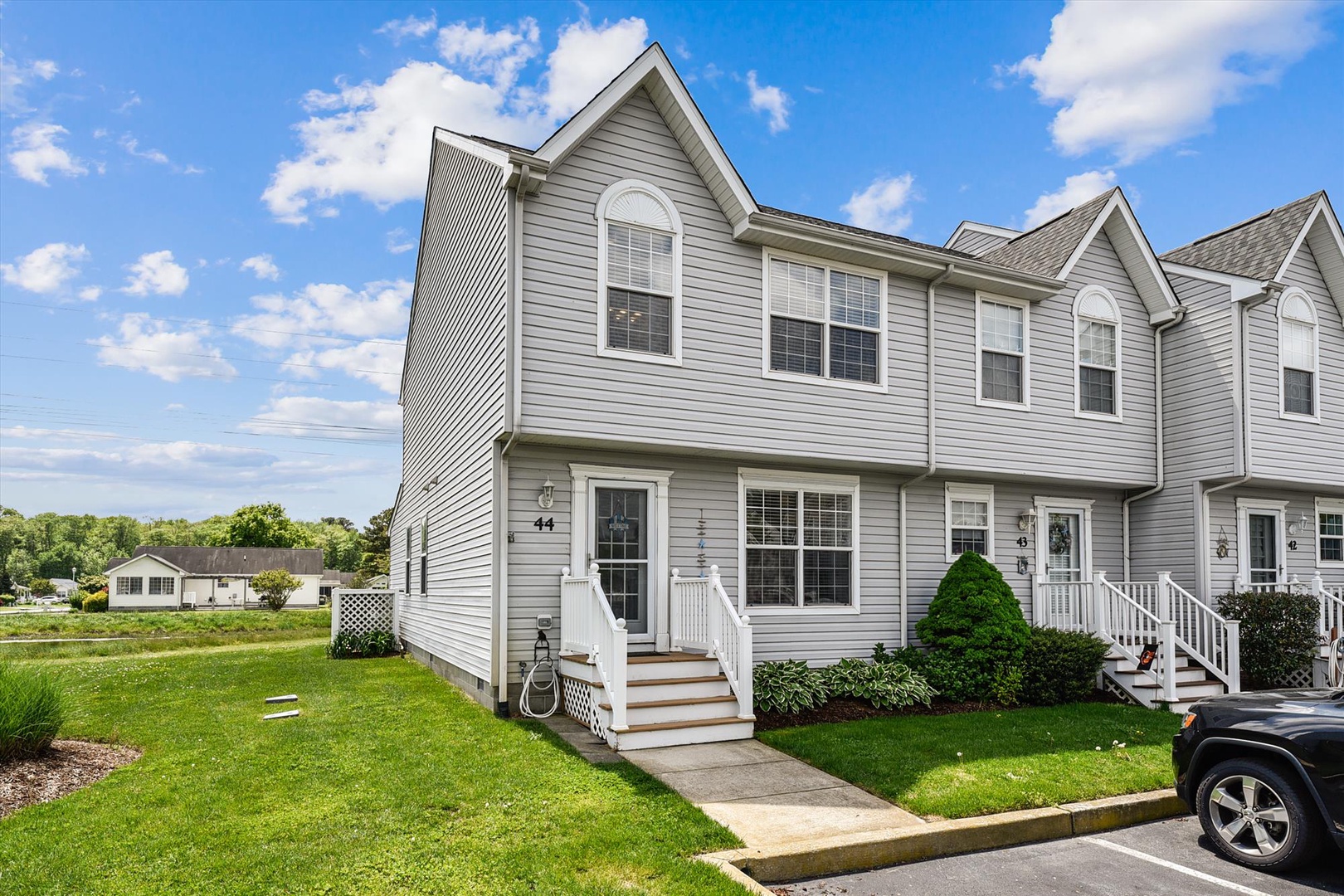 This modern townhouse features gray siding, arched windows, and a welcoming entrance with white railings. The property sits in a well-maintained residential community with manicured lawns and convenient parking.