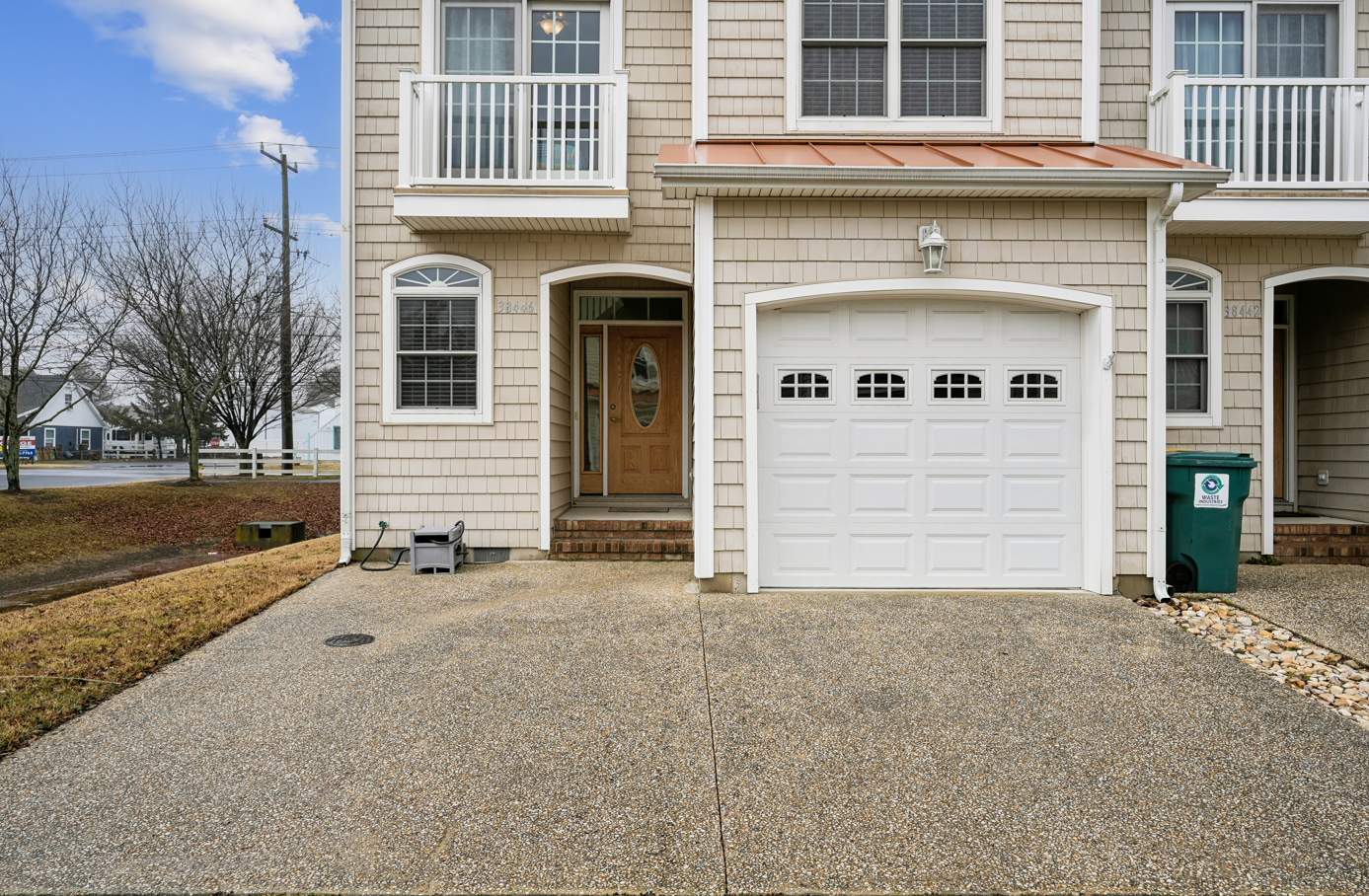 Charming coastal townhome featuring cedar shingle exterior, private garage, and welcoming entrance in a peaceful neighborhood setting.