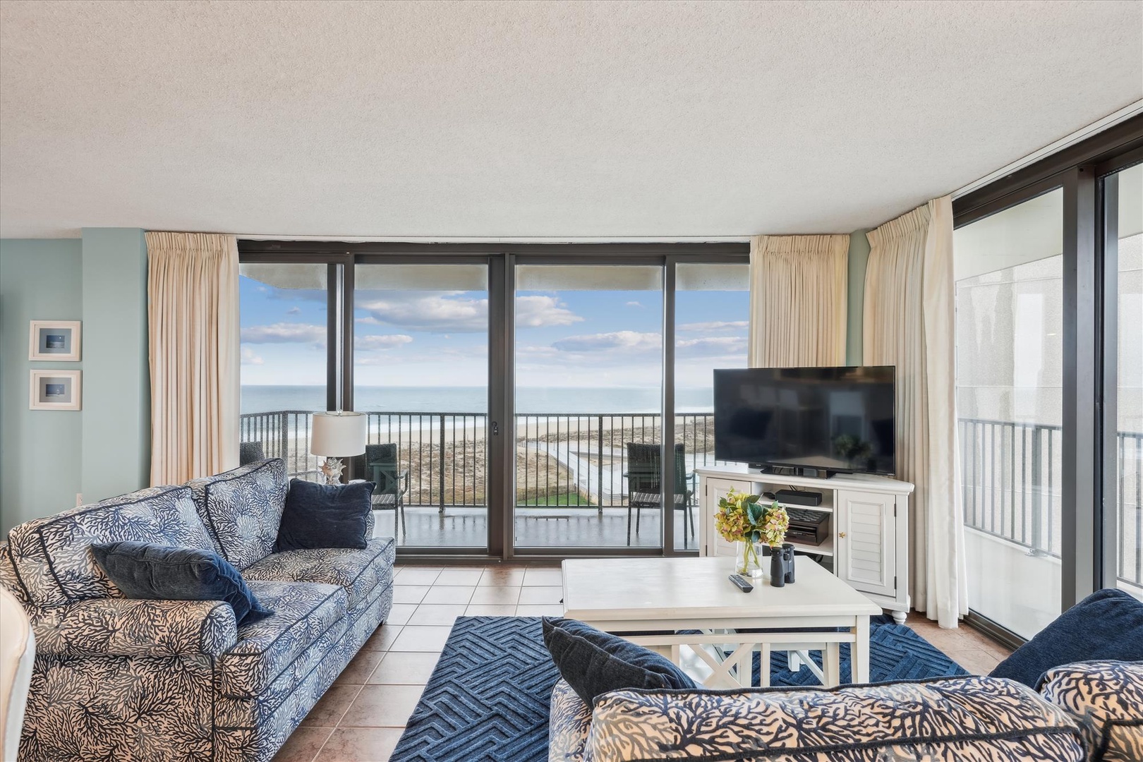 Unwind in your coastal living room where panoramic ocean views stretch endlessly beyond floor-to-ceiling windows, perfect for morning coffee or sunset relaxation.